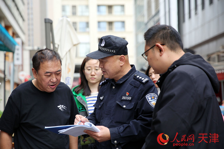 近日，天津公安南开分局体育中心派出所民警范星与社区网格员一起在时代奥城为商户做防范宣传。人民网记者 孙翼飞摄